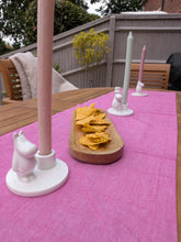 Load image into Gallery viewer, A pink table runner with matching pink and white Moomin-themed candle holders and a wooden chip bowl, set on an outdoor wooden patio table.