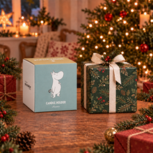 Load image into Gallery viewer, A Moomin-themed candle holder box sits on a wooden table beside a wrapped Christmas gift. The box is light blue and white with a Moomin character illustration and the text 'CANDLE HOLDER Moomin'.
