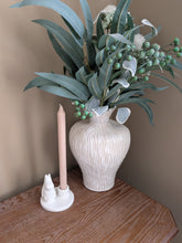 Load image into Gallery viewer, A textured off-white ceramic vase filled with eucalyptus leaves, white flowers, and green berries, styled on a wooden table next to a pink taper candle in a white holder against a beige wall.
