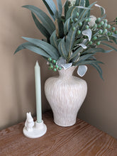 Load image into Gallery viewer, A decorative ceramic vase with a ribbed cream and gray texture, filled with eucalyptus branches and green berries, styled on a wooden table next to a white candle holder with a small rabbit figurine.
